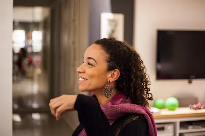 Renata Lage sorrindo de perfil em um ambiente acolhedor